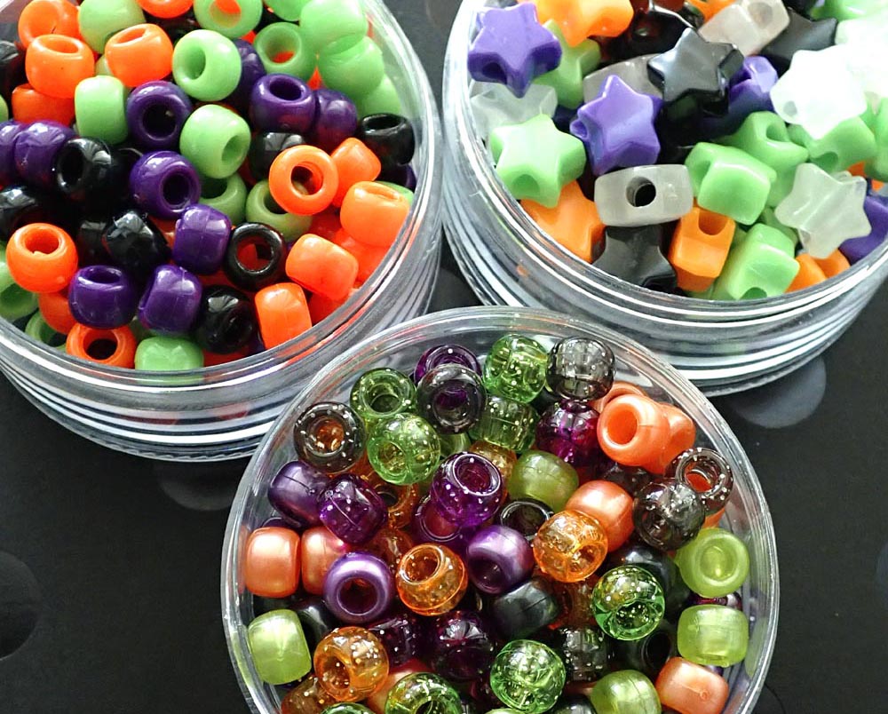 three clear containers filled with Halloween beads on a dark background